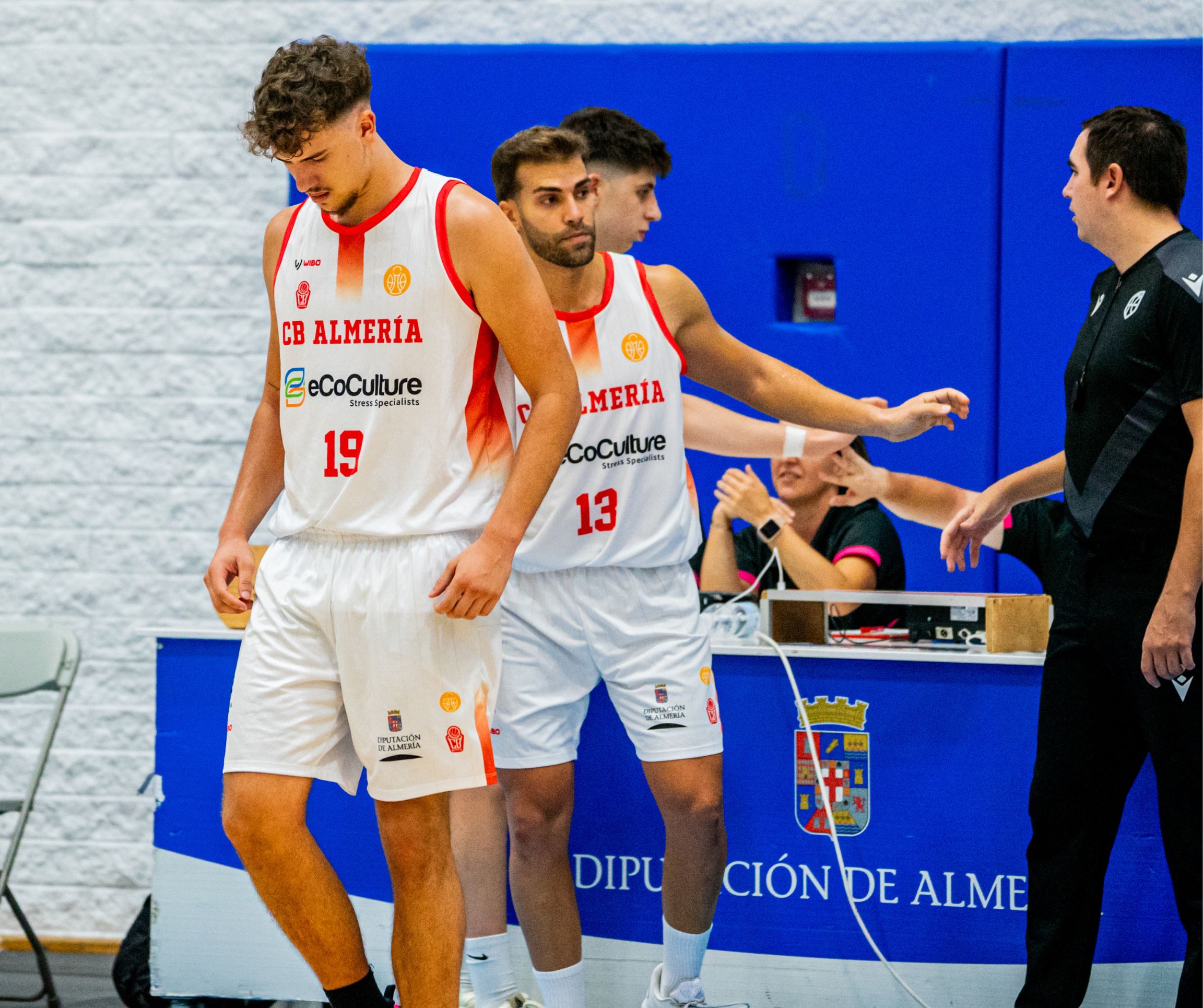 Jugadores del CB Almería de Tercera FEB, con los dorsales 19 y 13, junto a la mesa de anotación durante un partido de baloncesto